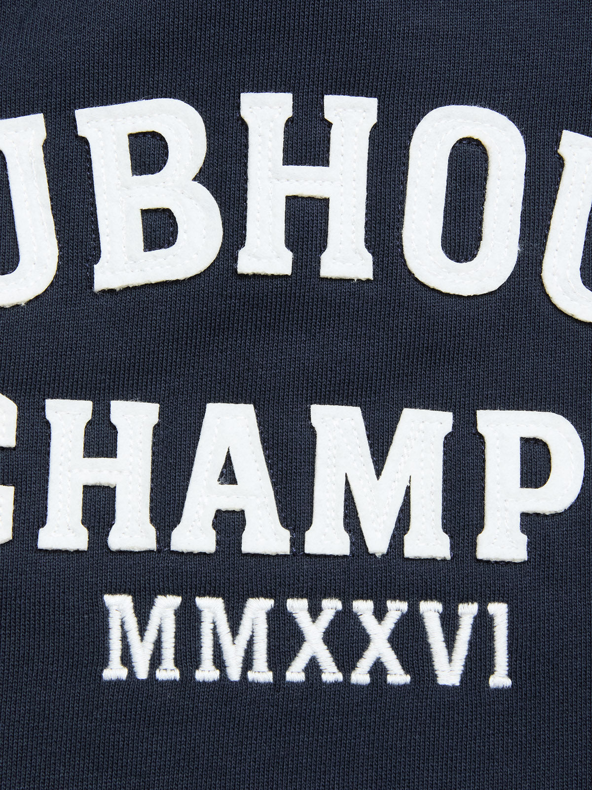 Close-up of navy blue cotton jersey fabric from the BGclubhouse Rugby Sweatshirt by Blue de Gênes, featuring large, bold white embroidered text reading “UBHOU CHAMP MMXXVI.” The classic lettering style evokes vintage athletic heritage, reminiscent of retro rugby sweatshirts.