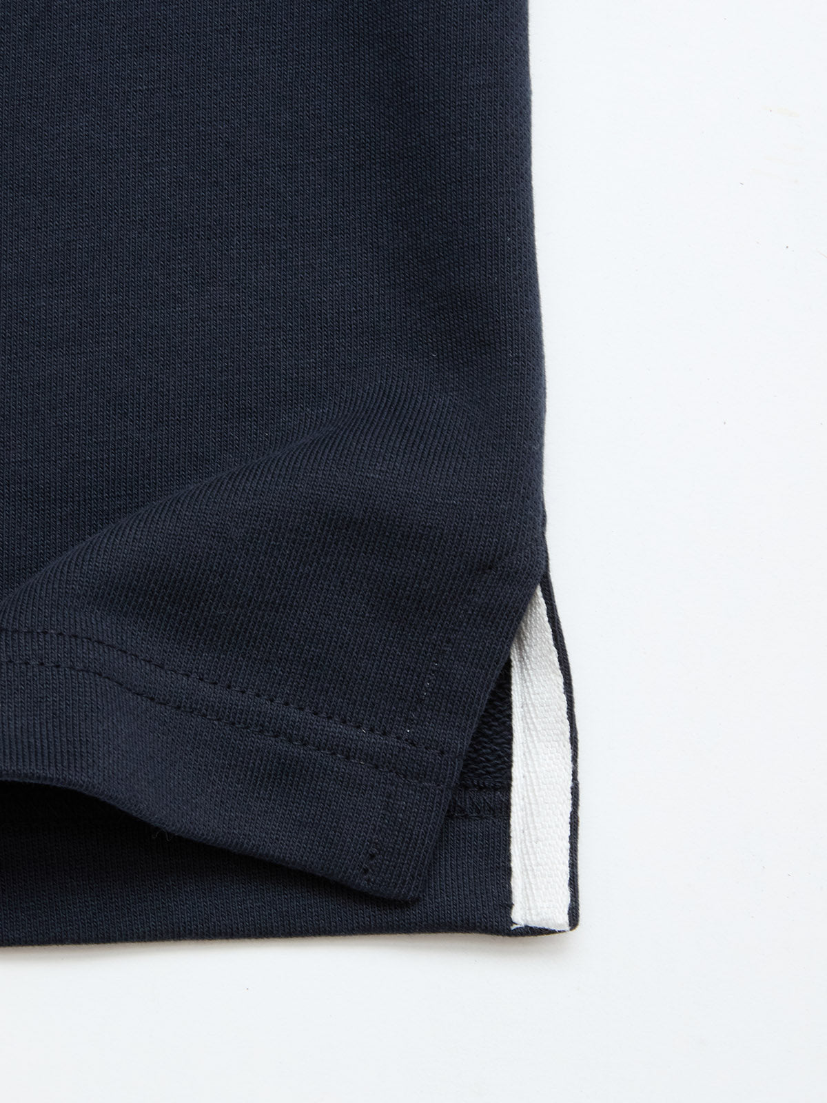 Close-up of the hem of the BGclubhouse Rugby Sweatshirt in navy by Blue de Gênes, crafted from soft cotton jersey and featuring a white fabric detail at the side vent, set against a light background—a refined piece from the Clubhouse Champs Collection.