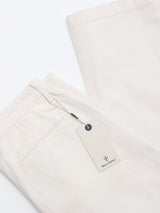 A pair of neatly folded BGpalco Twill Pants in Chalk by Blue de Gênes, featuring tapered legs and a back pocket. A rectangular cream tag with a small crest logo and the text “British Clothing” is attached by string.