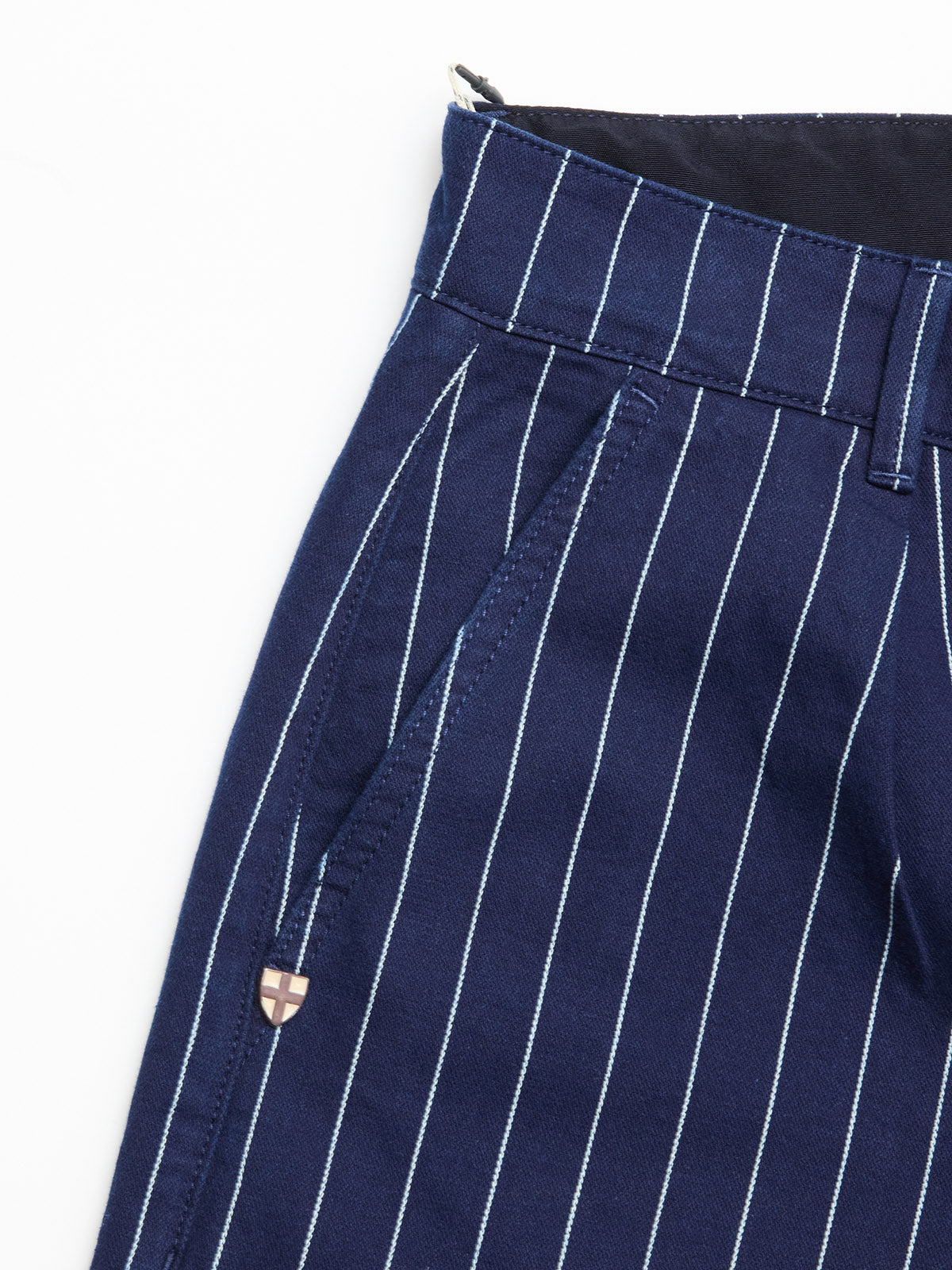 Close-up of Blue de Gênes BGcupra Toll Shorts in navy stripe, featuring white vertical pinstripes, a belt loop, side pocket, and a small metallic emblem near the seam.
