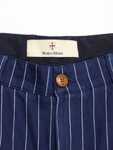 Close-up of the waistband of BGcupra Toll Shorts - Navy Stripe by Blue de Gênes, featuring a brown button and label with the brand's red and white shield logo—ideal inspiration for summer striped cotton shorts.