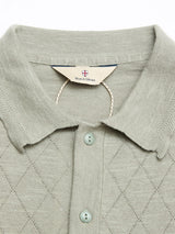 Close-up of the BGwally Diamond Polo in Shadow Green by Blue de Gênes, featuring diamond-patterned stitching on a light green cotton-linen blend, three buttons, and a Blue de Gênes tag inside the collar.