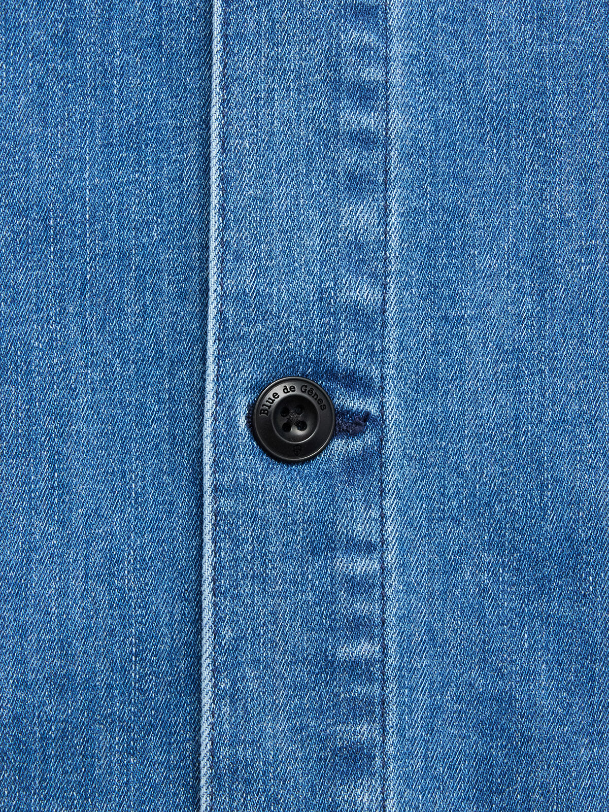 Close-up of the BGpontus Denim Overshirt - Used by Blue de Gênes, featuring blue cotton blend denim with a classic twill weave, visible vertical seam, and black button fastened through a buttonhole. Perfect for a relaxed fit.