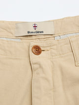 Close-up of the BGpalco Rodas Pants in pale khaki, crafted from a beige cotton-hemp blend, highlighting the brown button, belt loops, and an interior waistband label featuring a red and white shield with the Blue de Gênes logo.