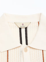 Close-up of the BGwalter S/S Cardigan - Chalk by Blue de Gênes, highlighting its cream knit collar with a button and branded label. Crafted from 100% cotton, this shirt showcases vertical stripes in black, brown, and beige on a textured fabric.