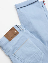 The BGpaulo Pavia Pant in Blue Fog by Blue de Gênes is shown folded on a white background, featuring a brown leather brand patch near the waistband and refined back pocket stitching inspired by vintage military chinos.