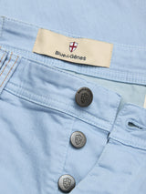 Close-up of Blue de Gênes BGpaulo Pavia Pant in Blue Fog with metal buttons, inner label beside a red and white shield logo, and pockets detailed by orange stitching for a classic, vintage-inspired look.