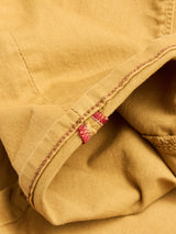 Close-up of the BGpaulo Pavia Pant - Sunflower by Blue de Gênes: yellow cotton stretch fabric with visible stitching, folded seam, and two short red stitches reminiscent of vintage military pant detail.