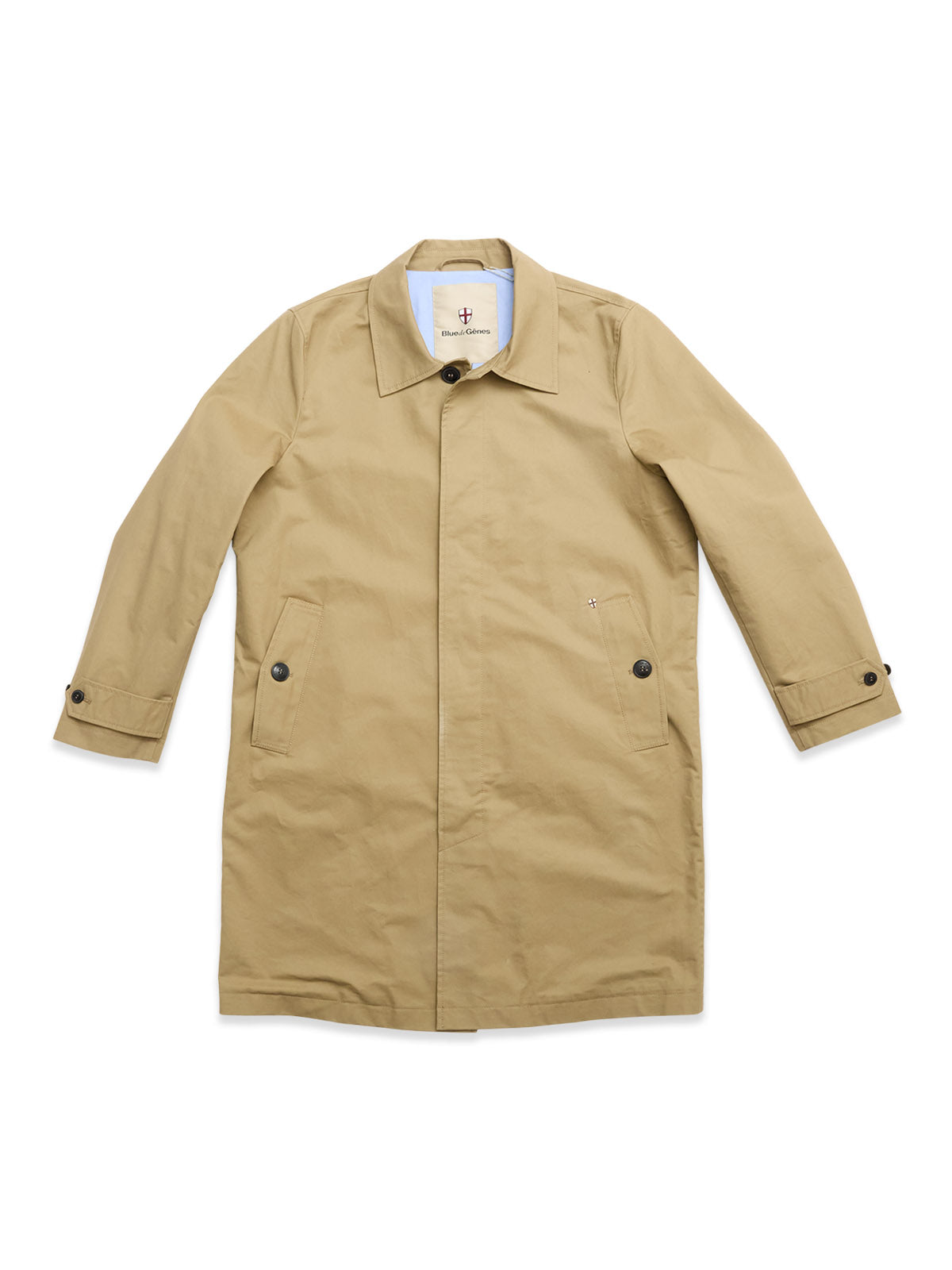 The BGjacques Coat by Blue de Gênes is a pale khaki, knee-length trench crafted from heavy cotton with a collar, buttoned front, two flap side pockets, and buttoned cuffs, displayed flat on a white background.