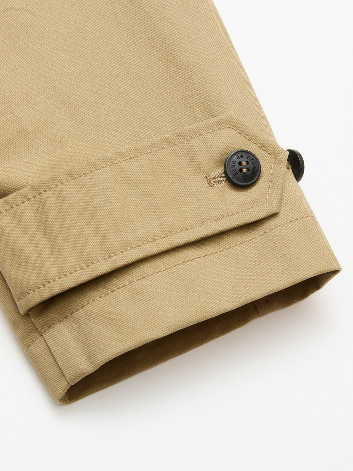 Close-up of the cuff of the Blue de Gênes BGjacques Coat in Pale Khaki, showing heavy cotton fabric, a black button, and a stitched fabric strap, set against a white background.