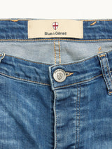 Close-up of the BGrepi Misto Jeans - Med Used by Blue de Gênes, showcasing blue denim with a metal button embossed with the Blue de Gênes name and shield logo, plus the brand label visible inside the waistband—a true reflection of classic design and craftsmanship.