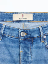 Close-up of the waistband of BGvinci Hera Used Jeans by Blue de Gênes, showing a label with red and white shield logo above the fly, silver branded button, and classic five-pocket styling in comfort stretch denim.