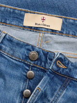 Close-up of BGvinci Hera Used Jeans - Used by Blue de Gênes in mid blue wash, regular fit with visible buttons, comfort stretch denim, gold stitching, and a Blue de Gênes label on the waistband.