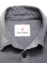 Close-up of the Nagano Overshirt in Dark Slate by Blue de Gênes, crafted from soft moleskin cotton, with a visible white collar label featuring the Blue de Gênes name and a red and white shield logo above it.