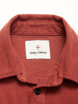A close-up of the Nagano Overshirt in Henna by Blue de Gênes, showing a visible white label inside the collar with the brand name and a red shield logo featuring a cross.