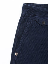 Close-up of the Blue de Gênes Etsu Cord Chino - Navy, highlighting its diagonal front pocket, buttoned flap, and a small embroidered shield patch near the pocket. Crafted from 7-wale corduroy fabric with a visible ribbed texture, these chinos offer a relaxed regular fit.
