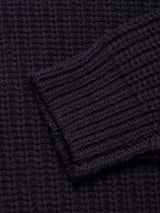 Close-up of the dark navy ribbed knit fabric of the Yomaha Halfzip Knit by Blue de Gênes, showcasing its textured pattern. The image focuses on a folded edge or sleeve, emphasizing the thick, cozy material characteristic of this chunky knit jumper.