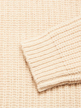 Close-up of the Yomaha Halfzip Knit - Fungi by Blue de Gênes, showcasing its beige, chunky knit texture with a ribbed cuff overlapping the body. The detailed knitted pattern, crafted in a cozy wool blend, highlights the signature Yomaha style.