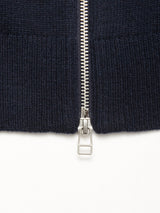 Close-up of a silver zipper partially unzipped on navy wool blend knit fabric, with the pull centered at the bottom on a white background—showcasing a detail from Blue de Gênes' Nuvali Polo Cardigan - Navy.