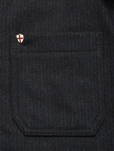 A close-up shows the dark denim pocket of the Vincenzo Solid Jacket by Blue de Gênes, with a small pin featuring a white shield and red cross above it, adding subtle detail to this relaxed fit Dark Navy jacket.