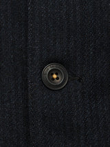 Close-up of a black, four-hole button with "Blue de Gênes" embossed on the edge, sewn onto dark textured fabric of the Vincenzo Solid Jacket - Dark Navy.