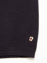 A close-up of the Toyama Knit L/S in Dark Navy by Blue de Gênes, showing its dark textured fabric and a small shield-shaped patch with a red cross near the hem.