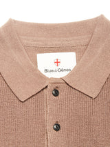 Close-up of the Porto Polo Knit - Fungi by Blue de Gênes, a light brown textured wool polo shirt featuring a collar and two buttons. The label inside the collar displays Blue de Gênes, accented by a small red and white shield logo above the text, capturing the essence of refined casualwear.