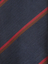 A close-up of the Nekutaki Tie #B - Navy Stripe by Blue de Gênes showcases its dark blue fabric with a subtle chevron pattern, accented by diagonal red and brown stripes—a refined design perfect for an elegant men’s accessory or a sophisticated navy and red striped tie.