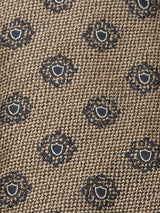 Close-up of the Nekutaki Tie #E - Sand Pattern by Blue de Gênes, showcasing its brown woven fabric with a subtle sand pattern weave and an elegant repeating circular blue and white geometric motif.