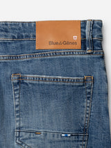 Close-up of the back pocket and waistband of Blue de Gênes BGvinci Girisha Used Jeans, made from comfort stretch denim, showing a brown leather brand patch and a small white and red shield emblem.
