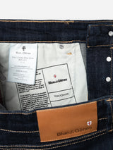 Close-up of the interior and waistband of Blue de Gênes BGvinci Girisha Rinse Jeans – Rinse Wash, featuring a leather brand patch, a product detail fabric label, and visible stitching on dark blue comfort stretch denim.