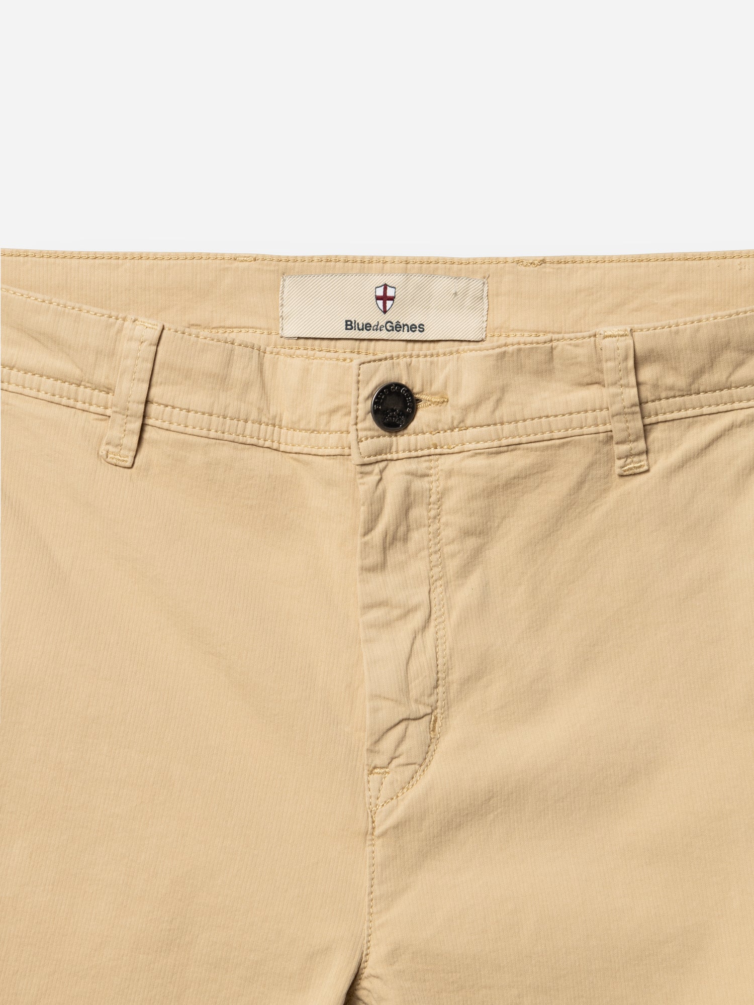 Close-up of the waistband and upper front of BGmenzo Vecchio Chino in Pale Khaki by Blue de Gênes, featuring comfort stretch, belt loops, a black button, and the Blue de Gênes label above the button.