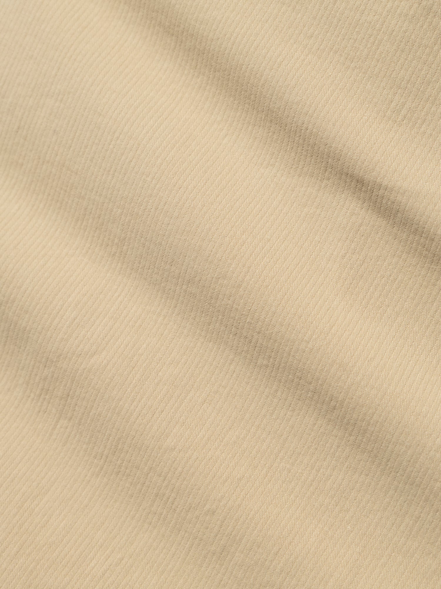 A close-up of Blue de Gênes' BGmenzo Vecchio Chino in Pale Khaki, showing its subtle diagonal ribbed texture and gentle shadows, reminiscent of classic vintage chinos.