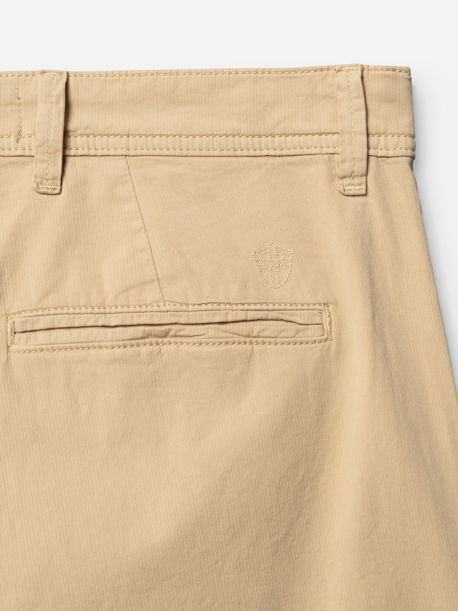 Close-up of the BGmenzo Vecchio Chino by Blue de Gênes in Pale Khaki, highlighting a belt loop, welt pocket, and embroidered shield logo above the pocket. The fabric offers a smooth, slightly textured finish for a classic vintage look.