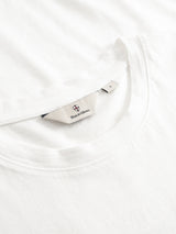 Close-up of a white Blue de Gênes BGoscar T-Shirt - Snow Fall, crafted from 100% cotton, featuring a visible beige label inside the collar with logo and “Save & Corona” text.