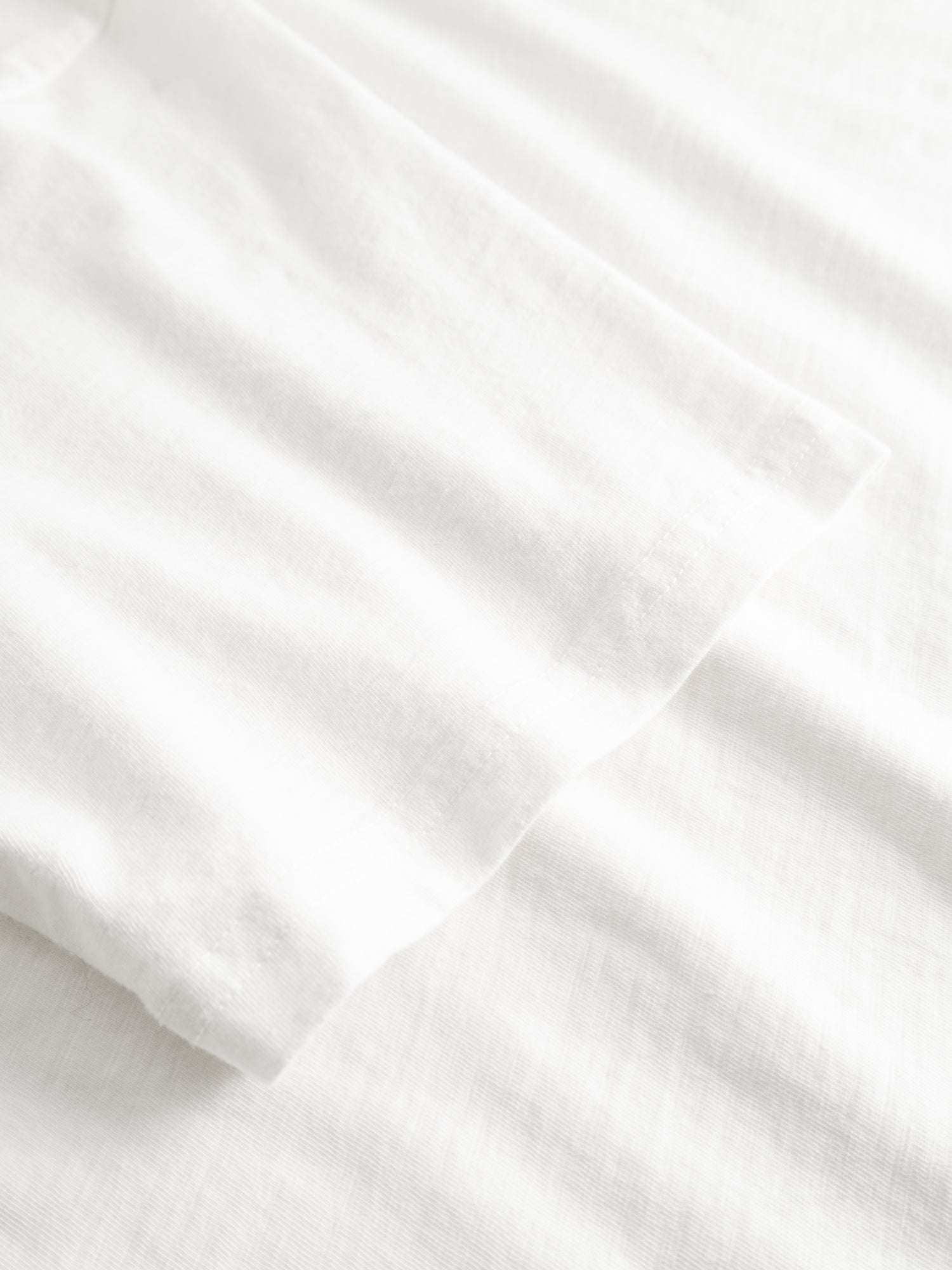 Close-up of a plain white BGoscar T-Shirt - Snow Fall by Blue de Gênes on a white textured fabric background, highlighting its soft and smooth 100% cotton material.