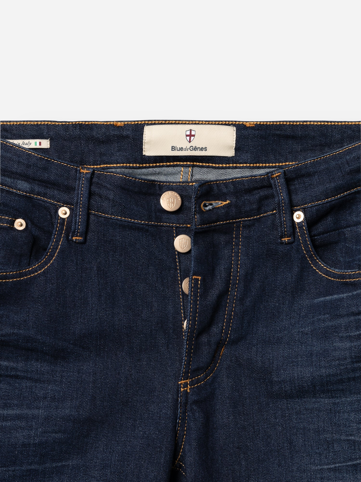 A close-up of BGvinci Pala Dark V2 Jeans by Blue de Gênes in dark blue stretch denim, featuring three metal buttons, orange stitching, and a branded inner label. Expertly crafted in Italy for a premium touch.