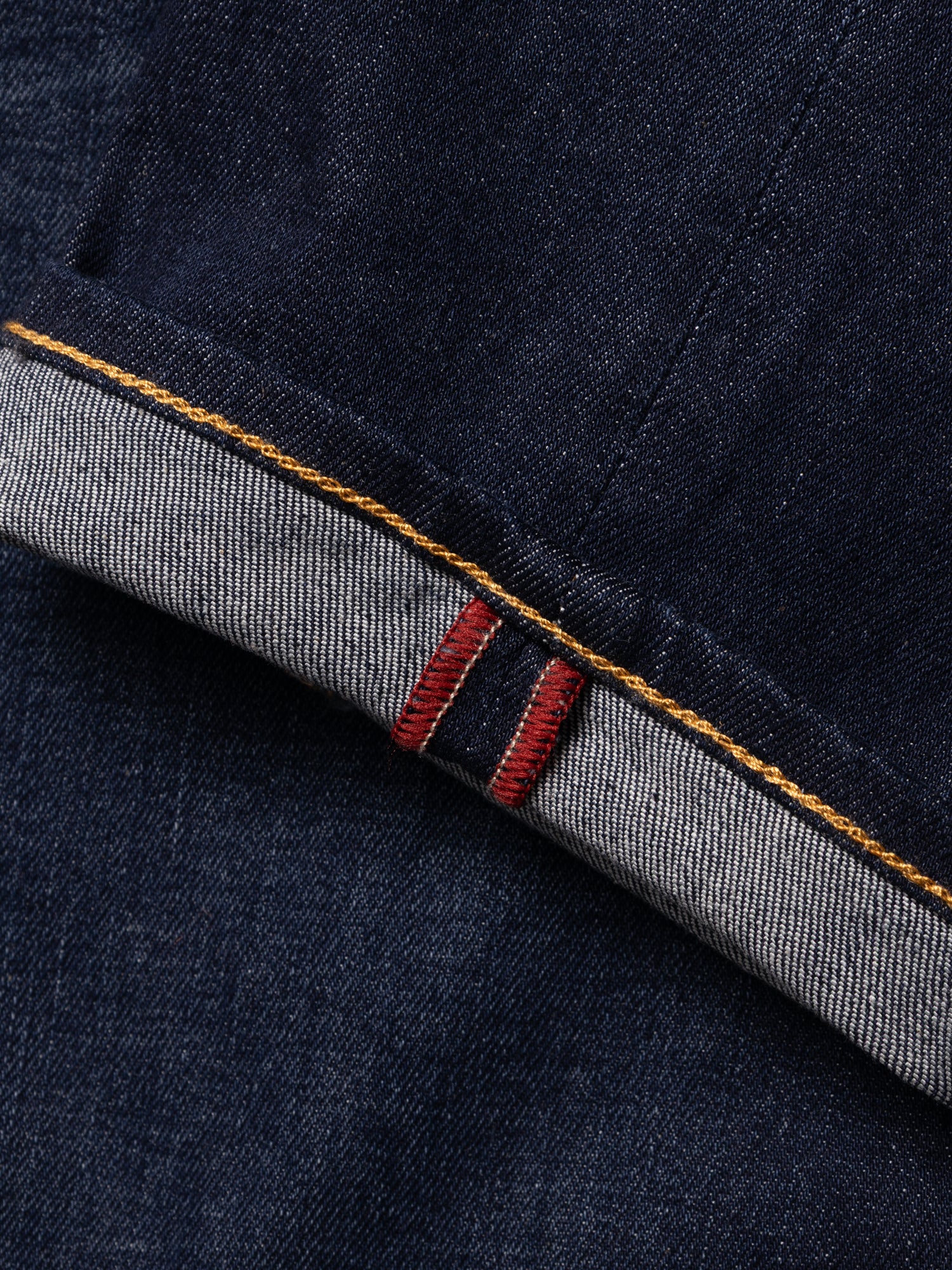 A close-up of the BGvinci Pala Dark V2 Jeans by Blue de Gênes in dark blue denim, crafted in Italy from selvedge fabric, highlighting the folded cuff with red and white stitching and a contrasting yellow seam.