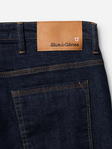 Close-up of BGrepi Dai V Dark V2 Jeans by Blue de Gênes in dark blue denim, with a brown embossed leather patch above the back pocket, white and red cross logo, and orange stitching on comfort stretch fabric.