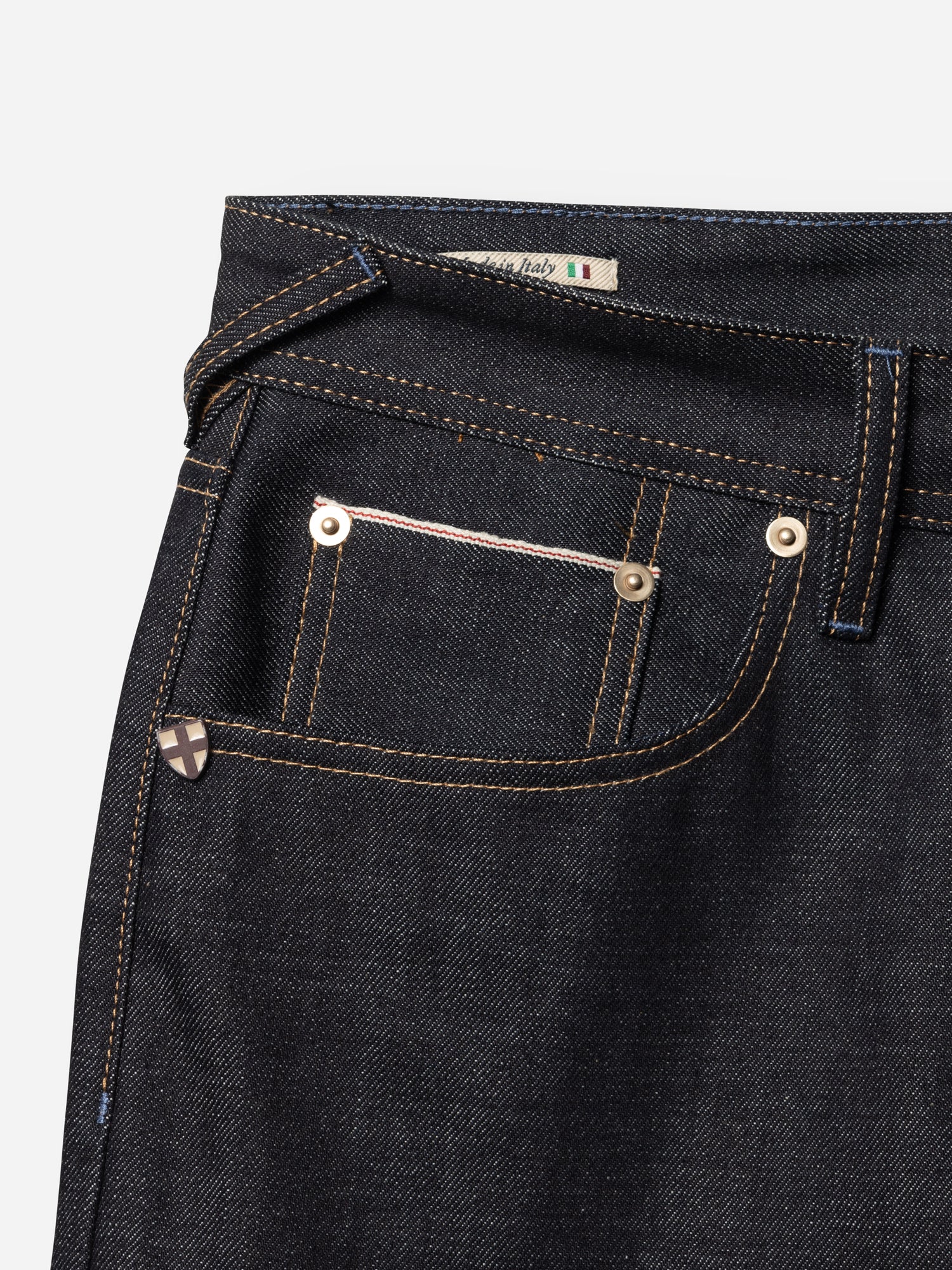 Close-up of the front pocket area of BGgiacomo Selvedge V2 Jeans - Raw Denim by Blue de Gênes, featuring dark blue rigid denim with brown stitching, metal rivets, and an Italian flag tag near the waistband—showcasing authentic made-in-Italy craftsmanship.