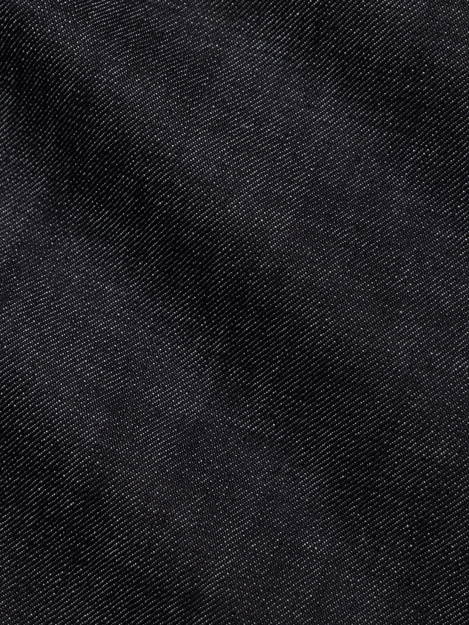 Close-up of the BGgiacomo Selvedge V2 Jeans - Raw Denim by Blue de Gênes, showcasing black selvedge denim with a distinctive diagonal weave, visible texture, and refined highlights and shadows—hallmarks of rigid denim jeans crafted with exceptional quality, reminiscent of relaxed loose fit Italian-made styles.
