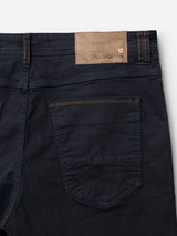 Close-up of the back of Blue de Gênes BGpaulo Pavia 1 V2 Chino in Midnight Blue, showing a brown leather patch with embossed branding, a small red and white shield, visible stitching, cotton stretch fabric, and a single back pocket.