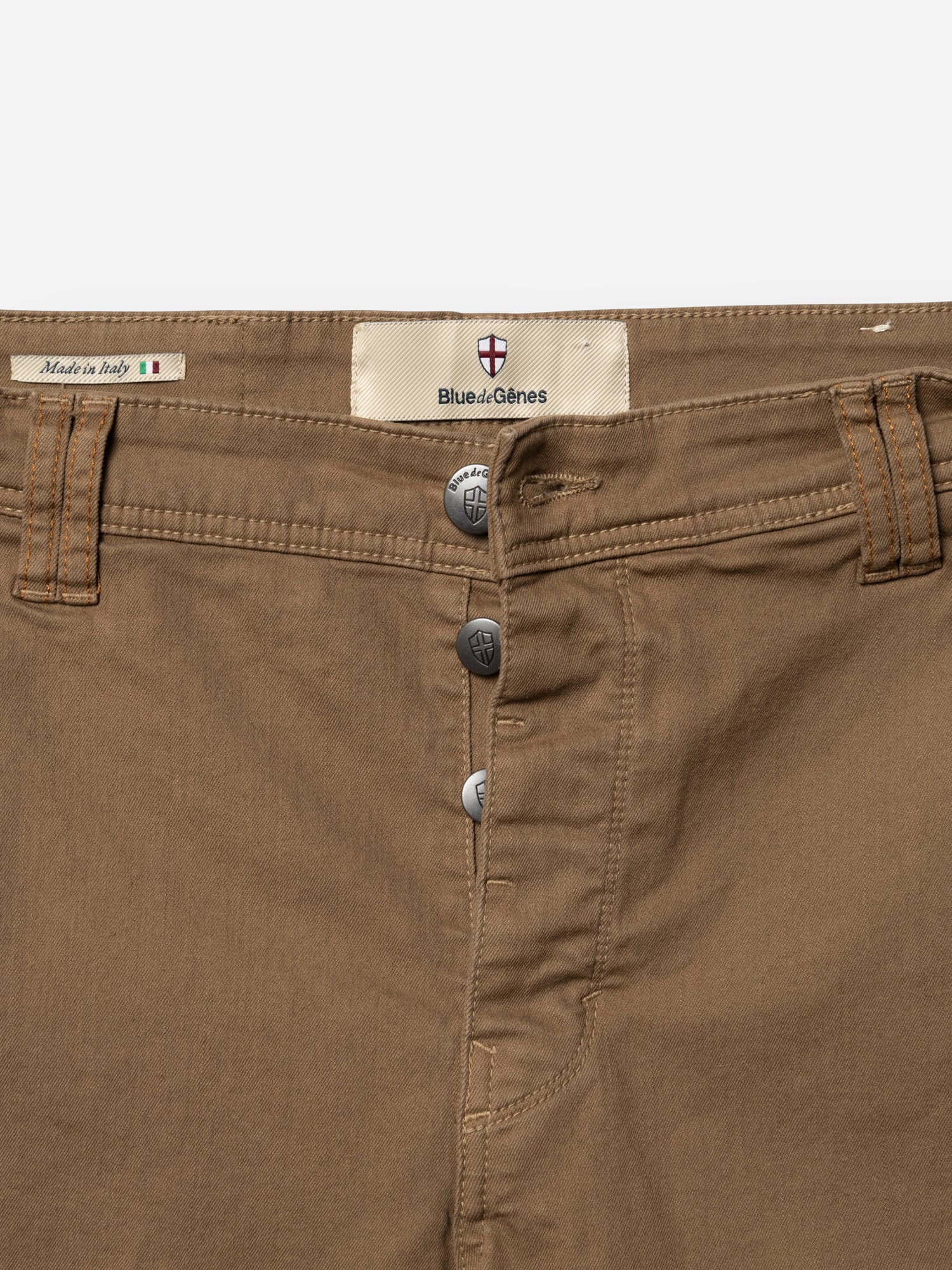 Close-up of fudge BGpaulo Pavia 1 V2 Chino by Blue de Gênes, featuring cotton stretch fabric, three visible buttons, belt loops, and a label above the waistband—crafted in Italy in vintage military style.