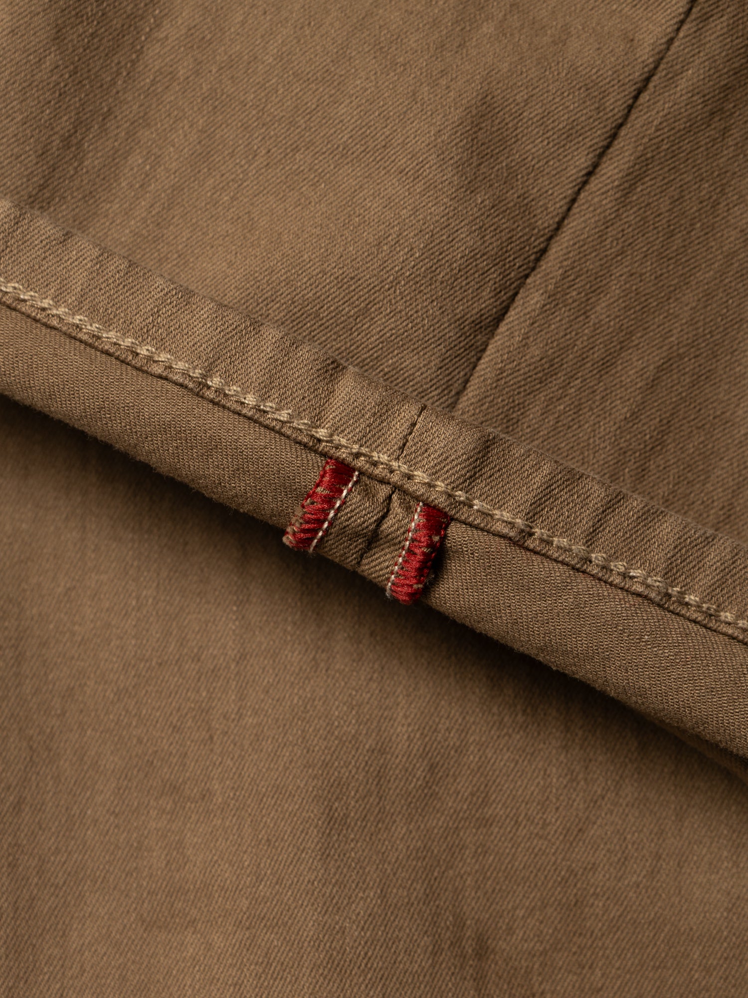 Close-up of Blue de Gênes BGpaulo Pavia 1 V2 Chino - Fudge shows brown cotton stretch fabric, visible stitching, and two red thread accents by the seam, highlighting its detailed texture and vintage military-inspired craftsmanship.