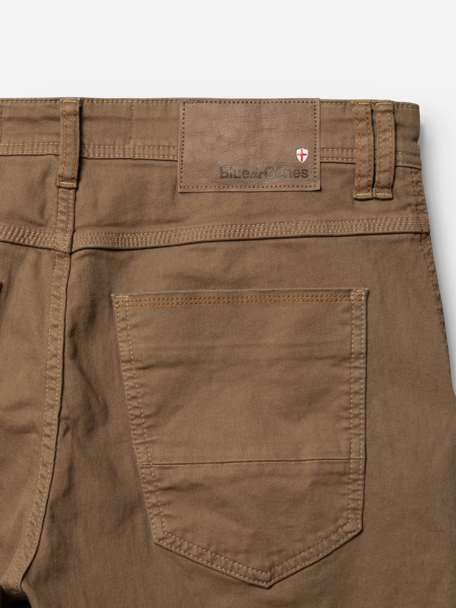 Close-up of the back of the BGpaulo Pavia 1 V2 Chino - Fudge by Blue de Gênes, showing a pocket, belt loops, and a leather patch embossed with Blue de Gênes and a small shield logo in the top corner.