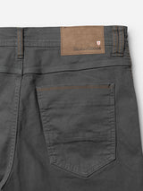 Close-up of the back pocket and waistband of the BGpaulo Pavia 1 V2 Chino in Charcoal by Blue de Gênes, featuring brown stitching and a tan leather patch with the Blue de Gênes logo and a small red and white crest on the waistband. Subtle nods to vintage military pants appear in the rugged yet refined design, while cotton stretch fabric ensures comfort with every wear.