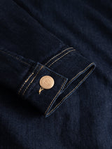 Close-up of the BGcosimo Trucker V2 Jacket by Blue de Gênes in dark blue denim, showcasing tan stitching and a metal button with engraved logo, inspired by classic western details and Italian craftsmanship.