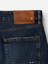 Close-up of the back pocket of denim blue BGvinci Arrow Jeans by Blue de Gênes, crafted from comfort stretch denim. Above the pocket, a brown leather patch features the Blue de Gênes name and a small shield logo on a white background. These regular fit jeans offer timeless style along with flexible comfort.