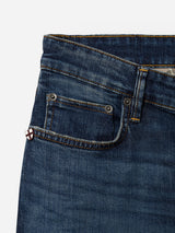 Close-up of the upper section of the BGvinci Hermina Jeans - Med Used by Blue de Gênes, crafted from comfort stretch denim in a dark blue wash, showcasing the waistband, front pocket, and small coin pocket accented with a metal rivet and a decorative patch featuring a red cross on a white background.