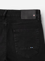 Close-up of the back pocket and waistband of the BGvinci TrueBlack Jeans in black denim, crafted from comfort stretch fabric, featuring a leather Blue de Gênes label and a small red and white shield emblem near the label.